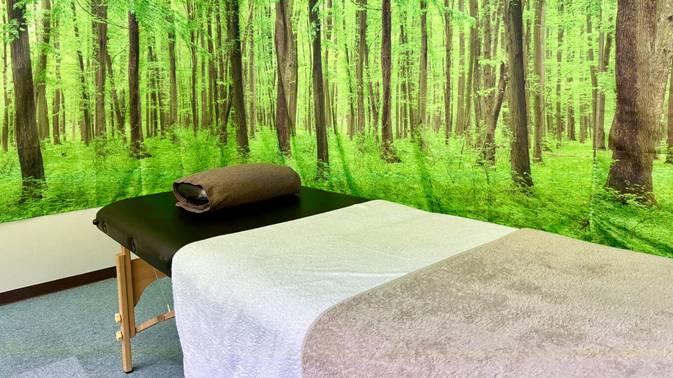 健楽足つぼの完全個室施術ルーム。森林の壁紙とリラックスできる施術ベッドがある空間。
